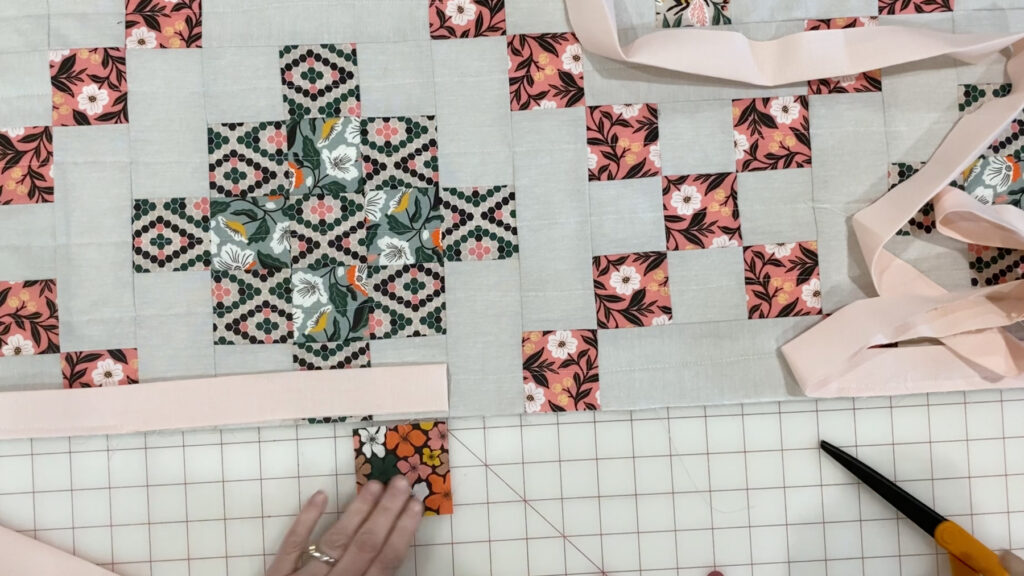 Measuring a 2 ½" overlap between the two binding tails using a fabric square as a guide.
