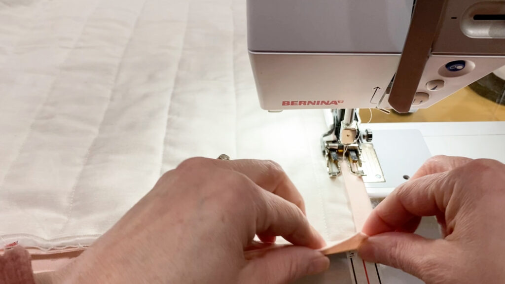 Turning the binding to the back of the quilt and stitching it down, mitering the corner.