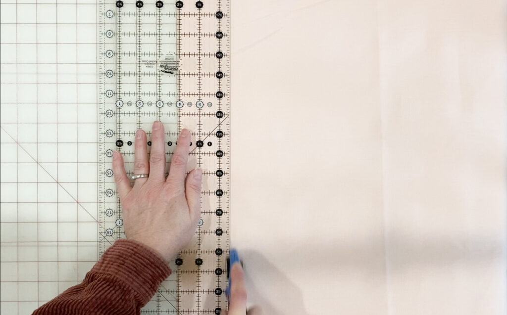 Cutting 2 ½" strips of binding fabric with a rotary cutter and quilting ruler on a cutting mat.