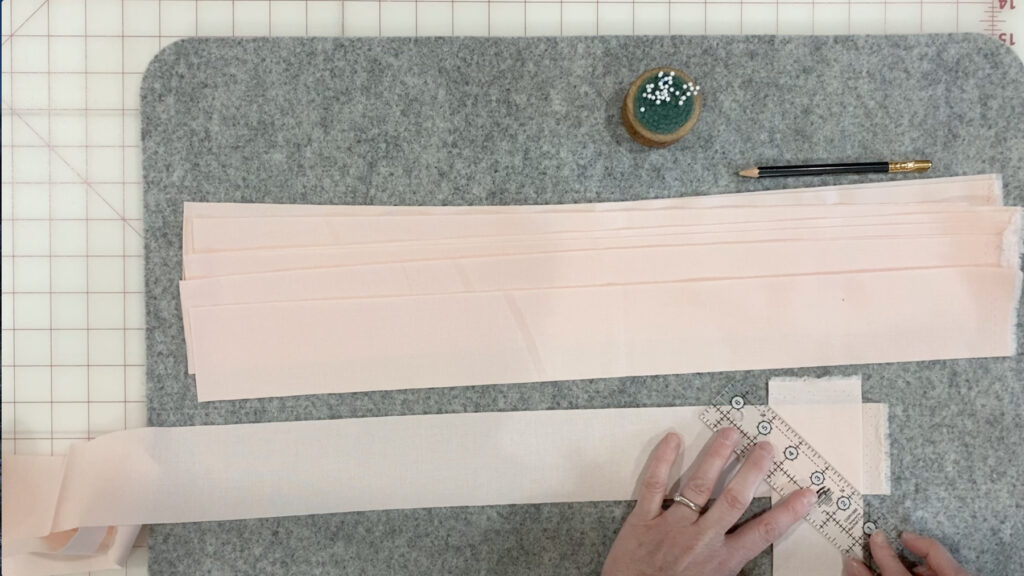 Aligning binding strips at a 90-degree angle with a ruler placed diagonally to draw the stitching line.