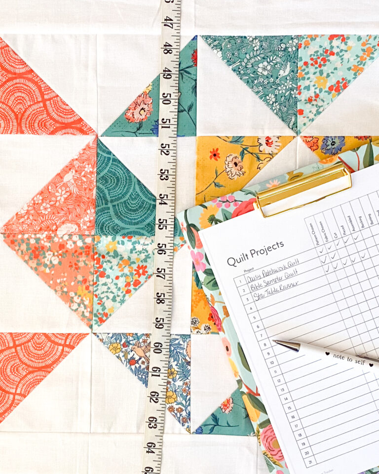 Free Quilt Project Tracker printed and displayed on a finished quilt at a cutting table