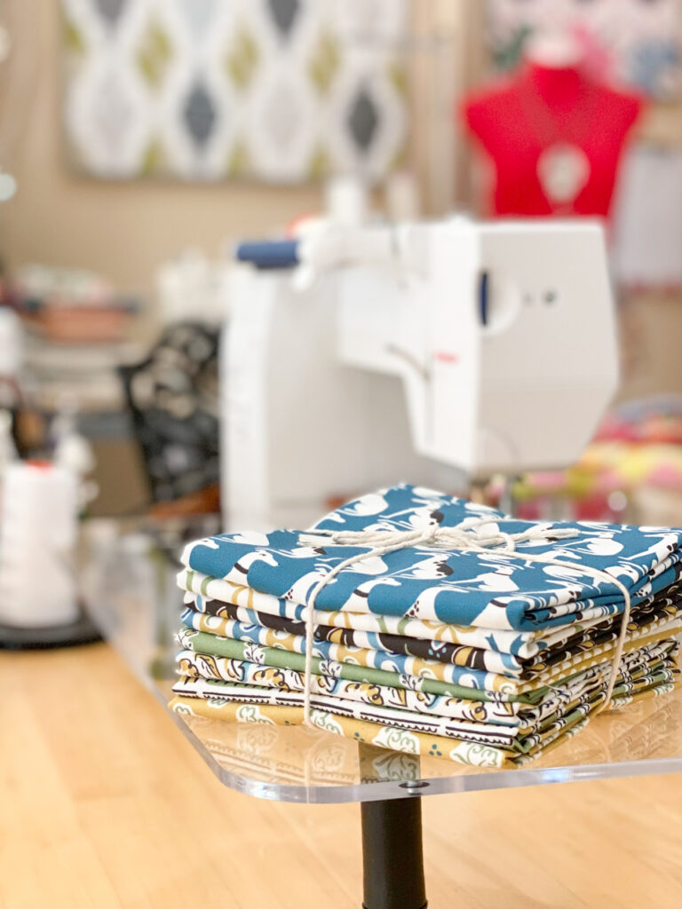 Fabric bundles used in Patches and Squares quilt pattern placed next to a sewing machine ready for piecing