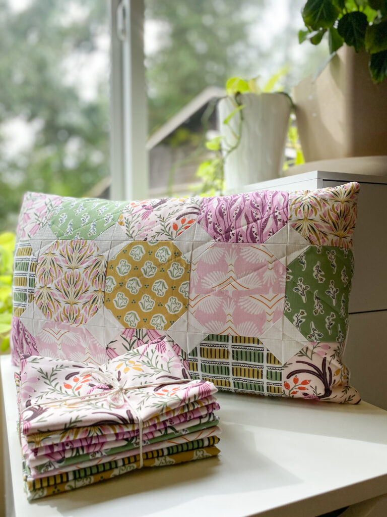 Quilted lumbar pillow with diamond straight line quilting displayed behind the Birds and Blooms fat quarter bundle featuring bird and floral fabric motifs