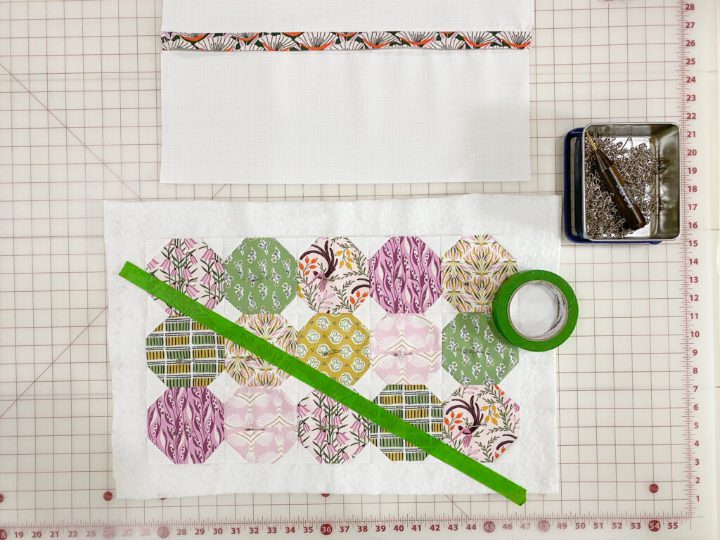 Quilt sandwich pinned with pillow top, batting, and backing, with painter’s tape placed across the top as a guide for straight line quilting